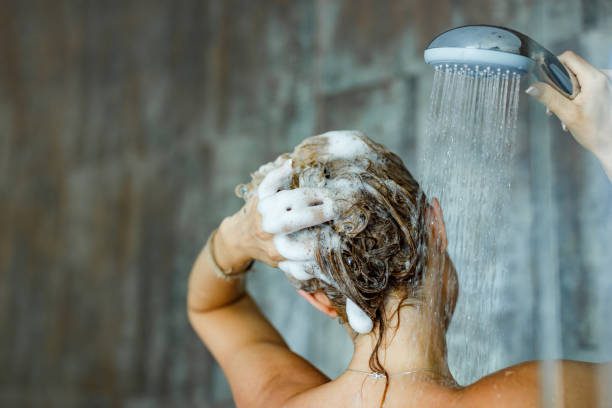 Back view of a woman washing her hair with a shampoo in bathroom.
